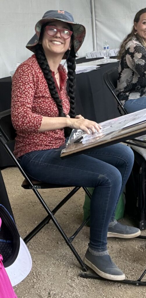 Simone drawing beneath a display of her caricature work
